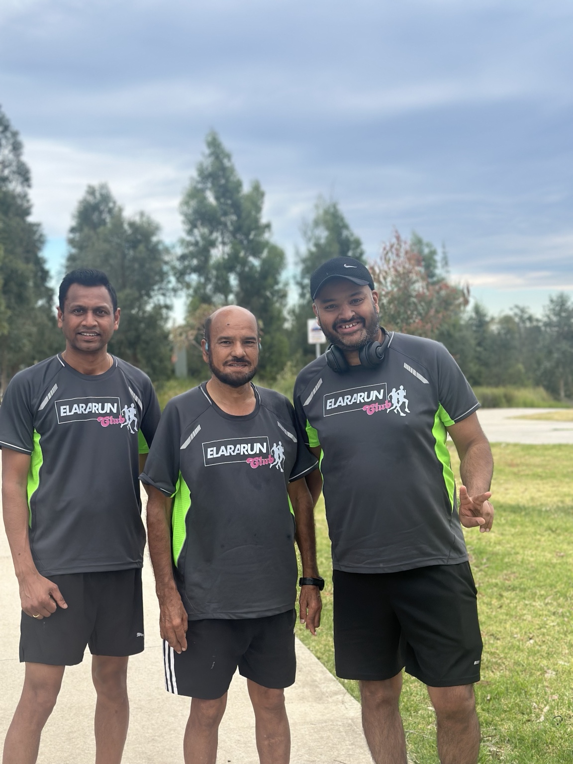 Three Elara Run Club members wearing the 2025 charcoal and green club shirt
